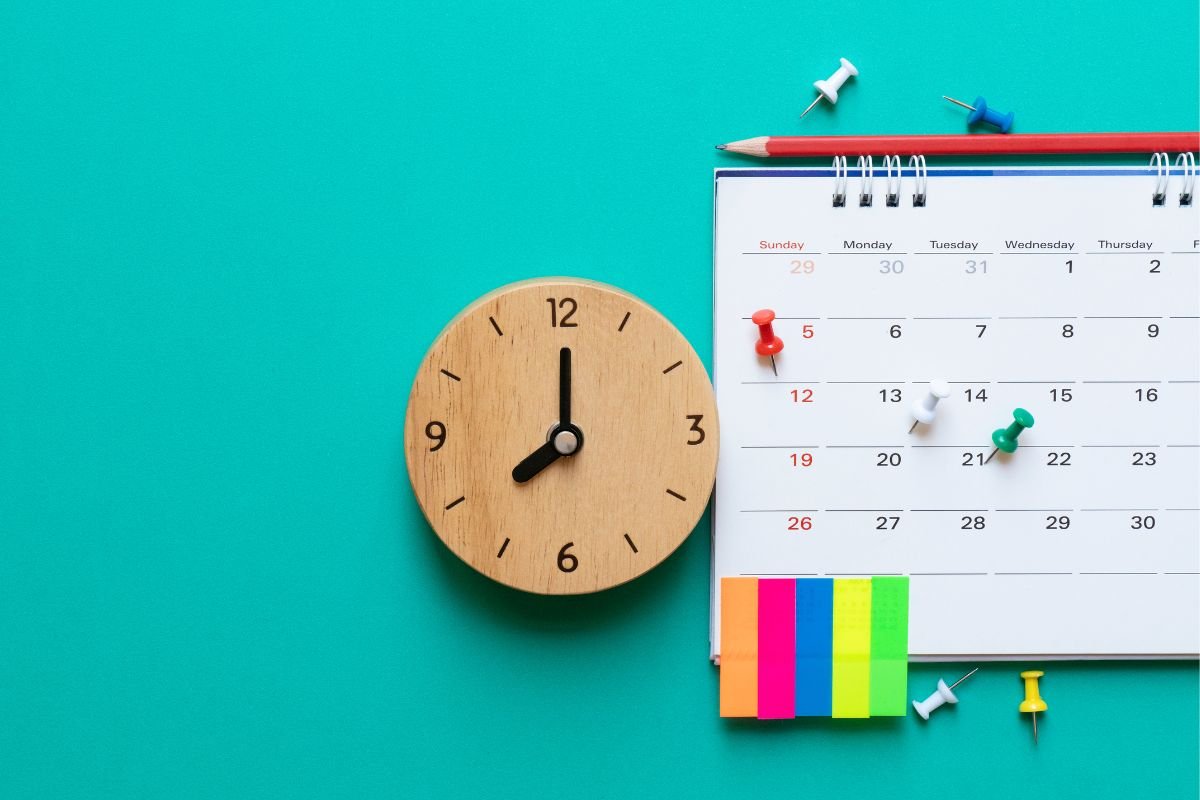 Calendário editorial jurídico ao lado de um relógio com com percevejos, posts-its e lápis.