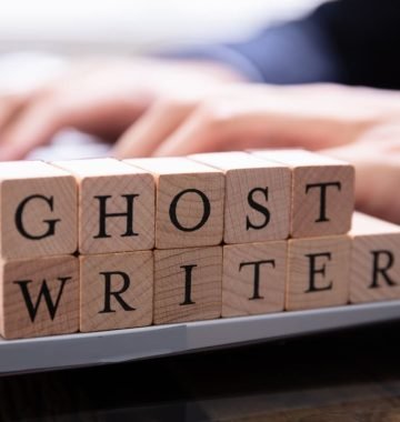 Ghost-writer-juridico Blocos de madeira com letras compondo a palavra ghost-writer em cima do teclado de um notebook em que um homem digita.