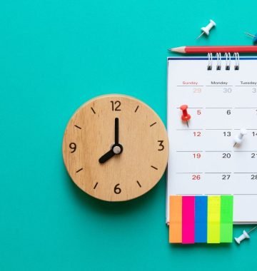 calendario-editorial-juridico Calendário editorial jurídico ao lado de um relógio com com percevejos, posts-its e lápis.